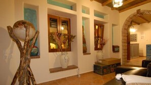 Uma sala de estar com sofá, uma escultura de madeira e duas janelas com plantas.