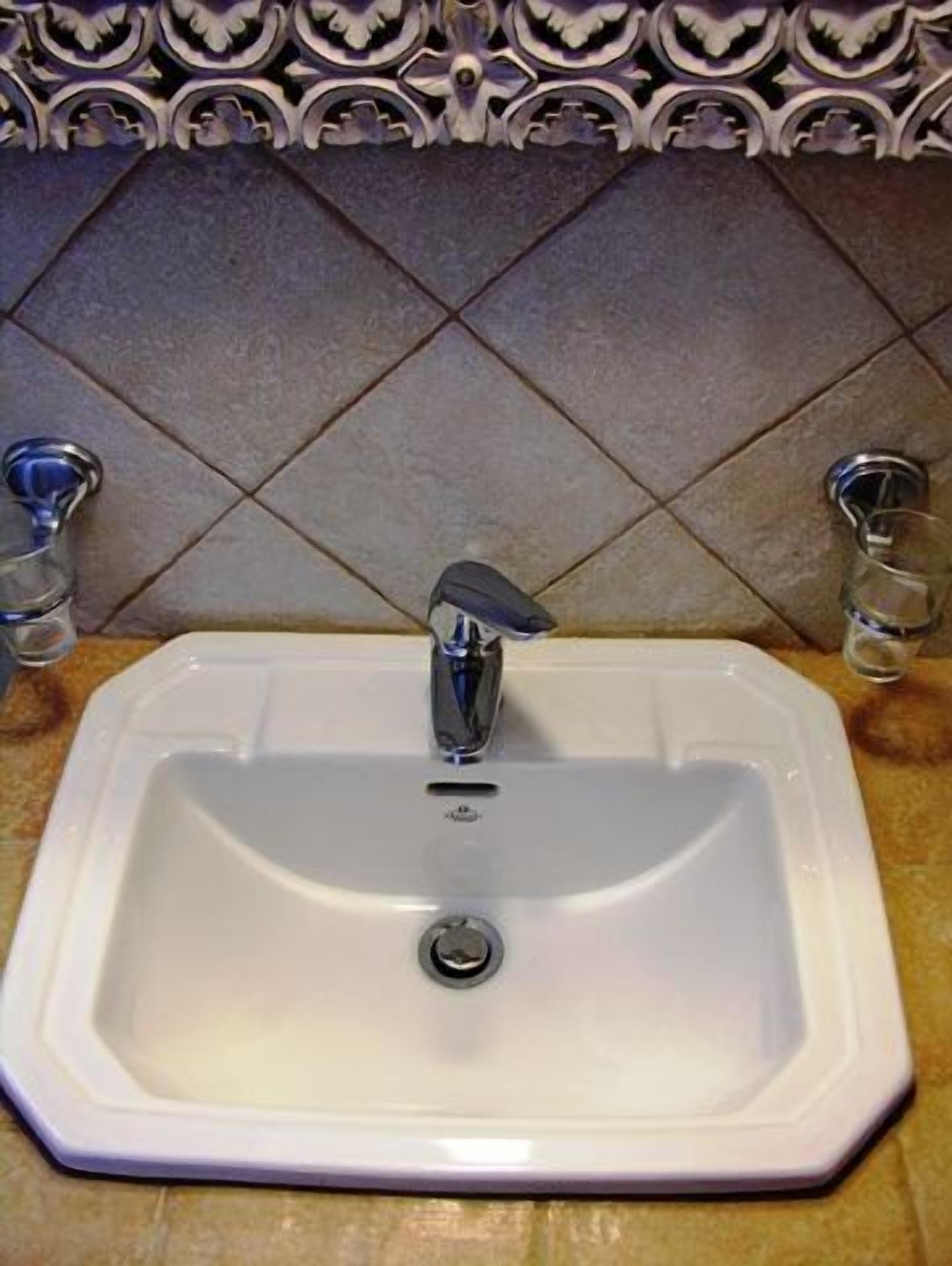 A white rectangular sink with a single faucet, set against a tiled backsplash with a diamond pattern.