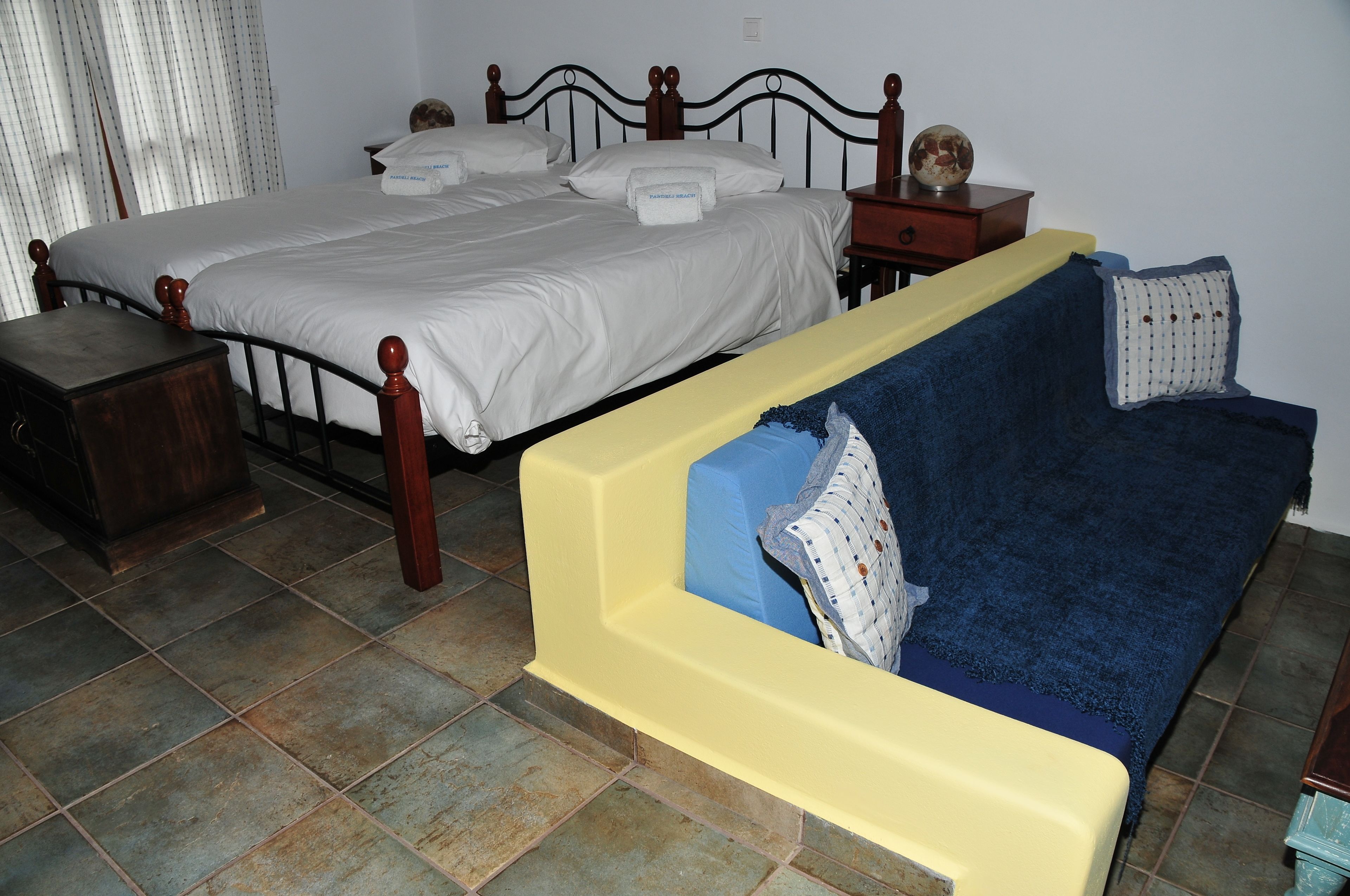 A bedroom with two beds, a wooden nightstand, and a yellow sofa.