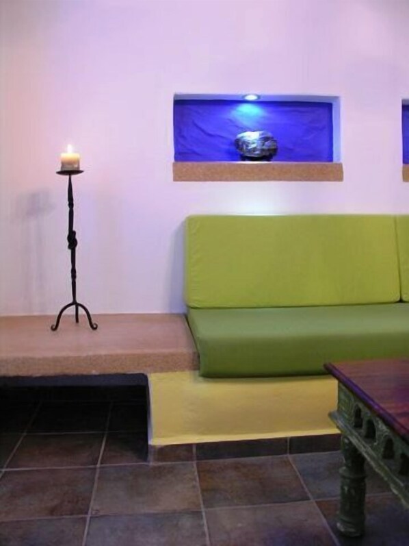 Una habitación con un sofá verde, una mesita pequeña, una vela sobre un soporte y una estantería con luz azul.