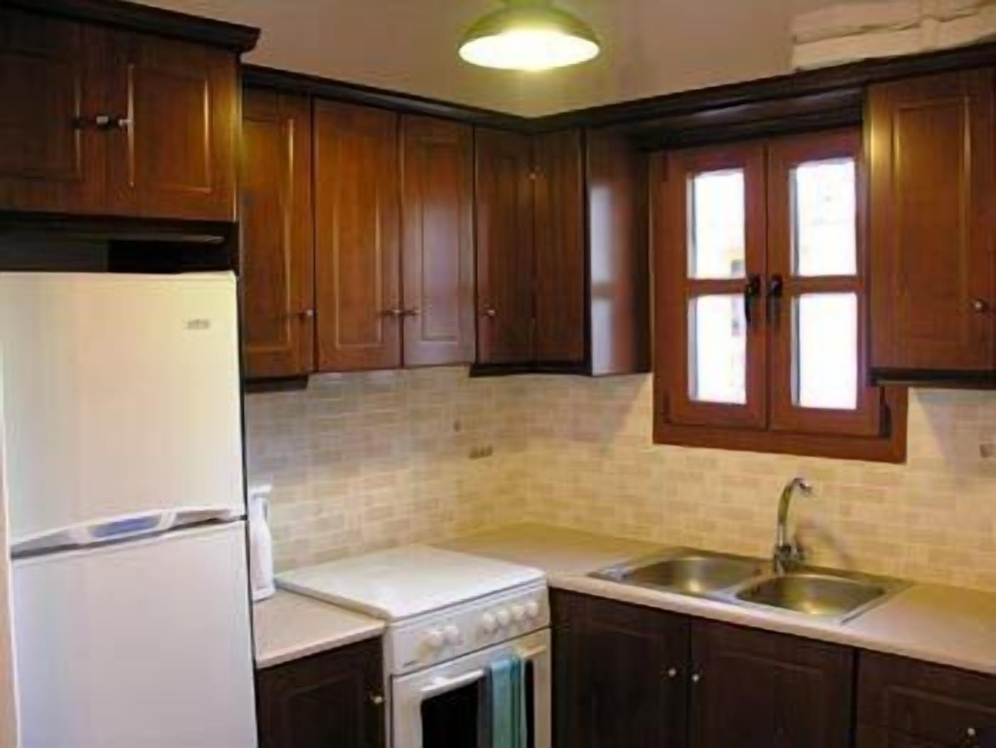 Een keuken met houten kastjes, een witte koelkast, een fornuis en een spoelbak.
