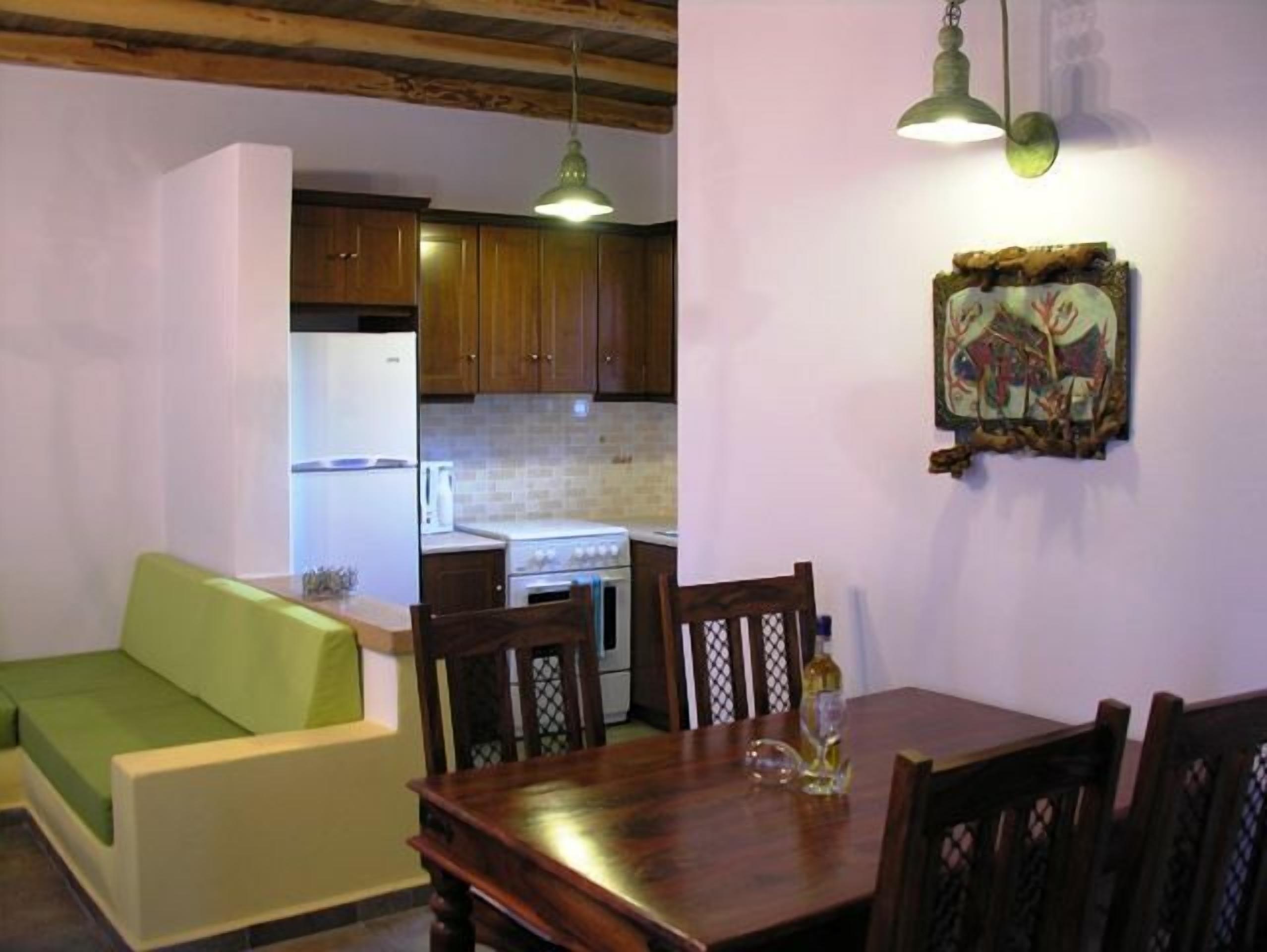 Une cuisine de taille réduite avec des meubles en bois, une table à manger avec des chaises et un canapé vert.
