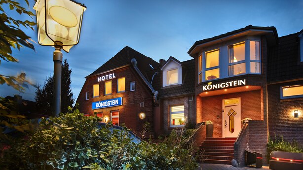 Un hotel con un cartel llamativo que dice 'HOTEL', un cartel que dice 'KÖNIGSTEIN' y una entrada bien iluminada con escaleras que conducen a la puerta.
