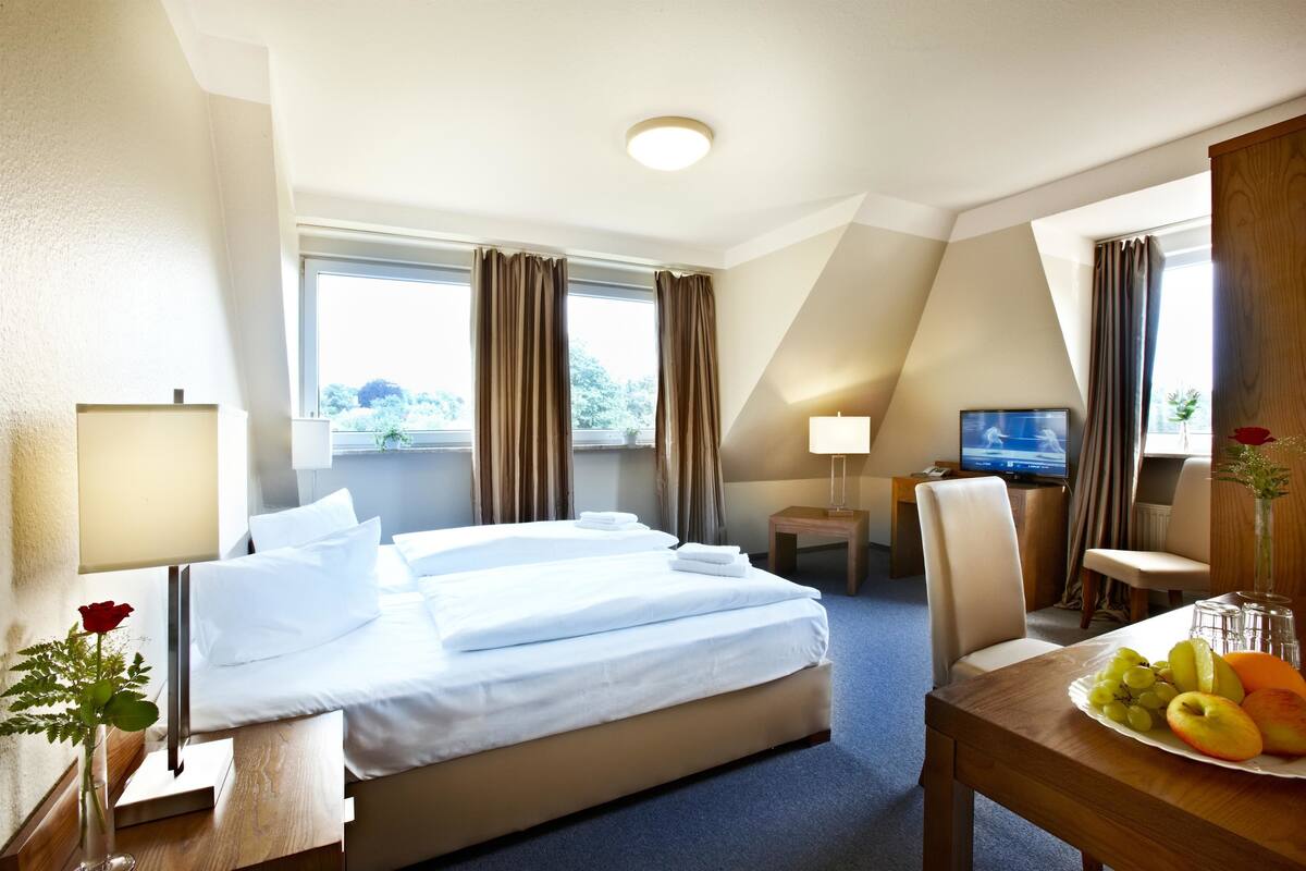 Habitación de hotel con cama, escritorio con una bandeja de fruta, televisión y ventana con cortinas.