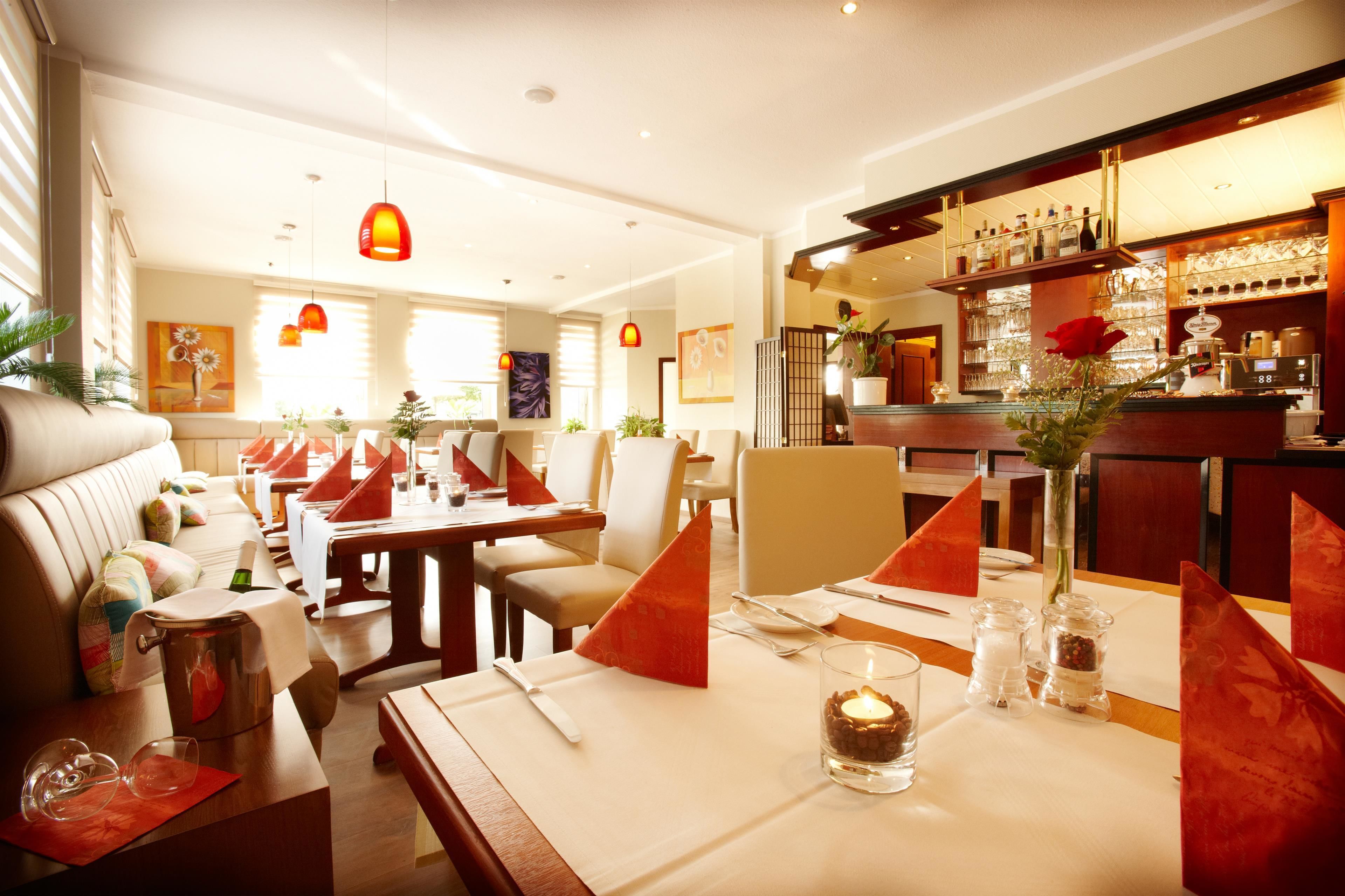 Un restaurante con mesas dispuestas para comer, una zona de bar con botellas y un espacio de estar con un sofá y sillones.