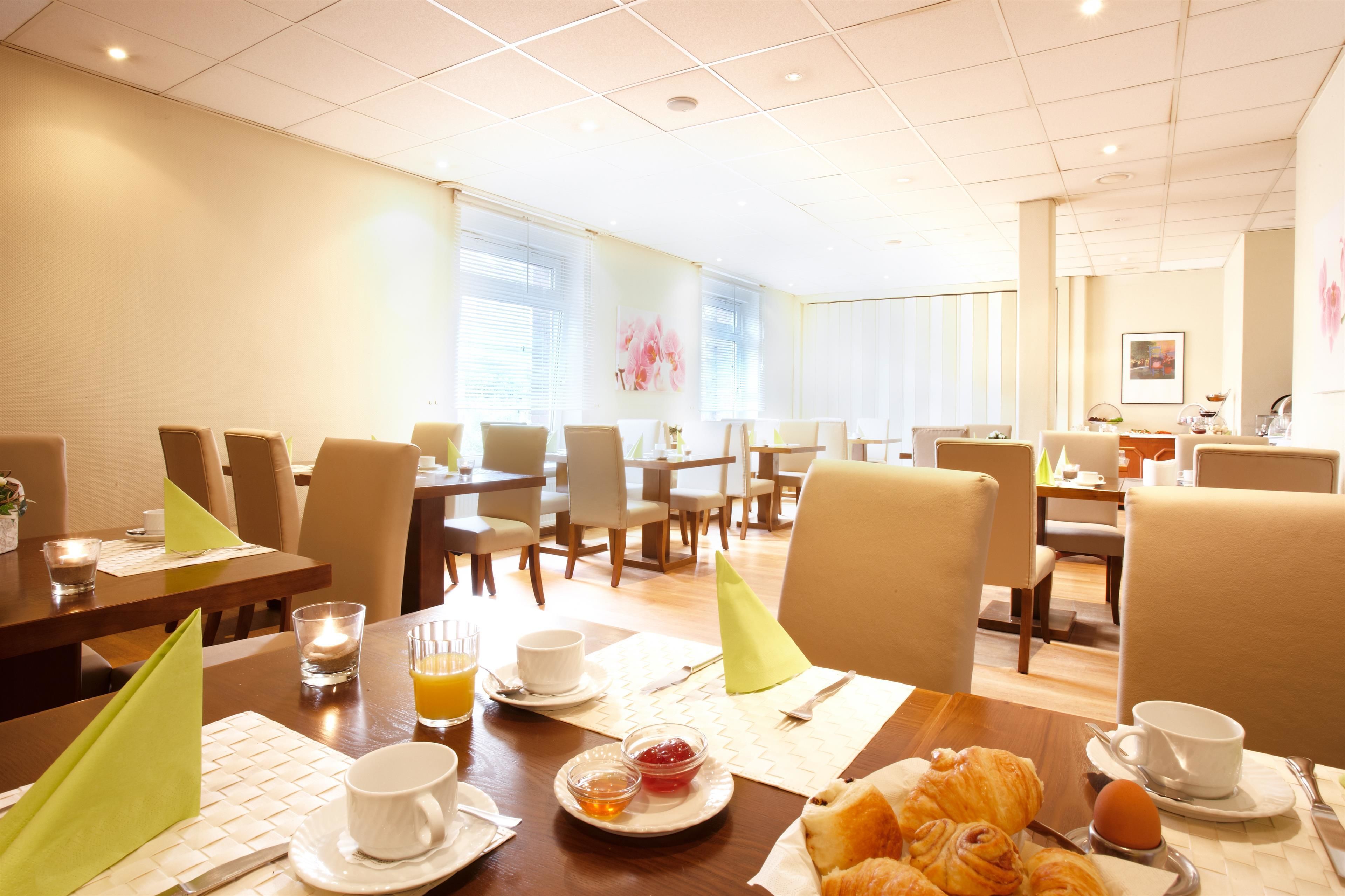 A hotel dining area with multiple tables, chairs, and breakfast items like croissants and orange juice.