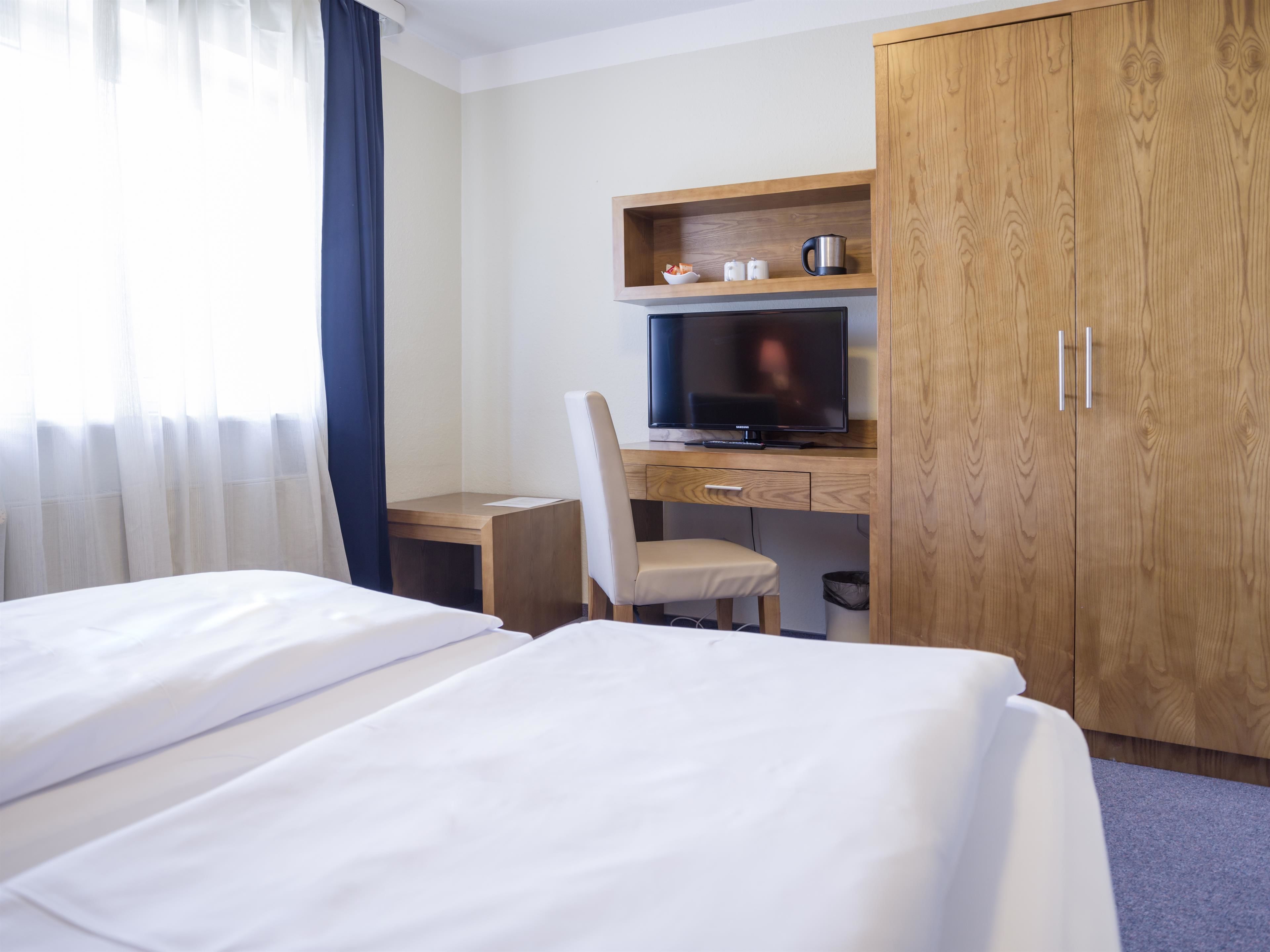 Een hotelkamer met twee bedden, een bureau met een computer, een televisie en houten kasten.