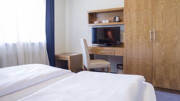 Een hotelkamer met twee bedden, een bureau met een computer, een televisie en houten kasten.