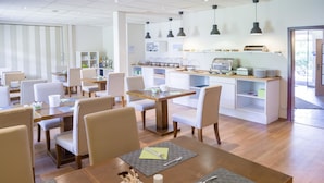 Un comedor moderno con mesas y sillas de madera, un espacio tipo bufé e iluminación colgante.