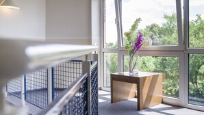 Un interior moderno con una mesita de madera, un florero con flores y vistas al verdor a través de amplias ventanas.