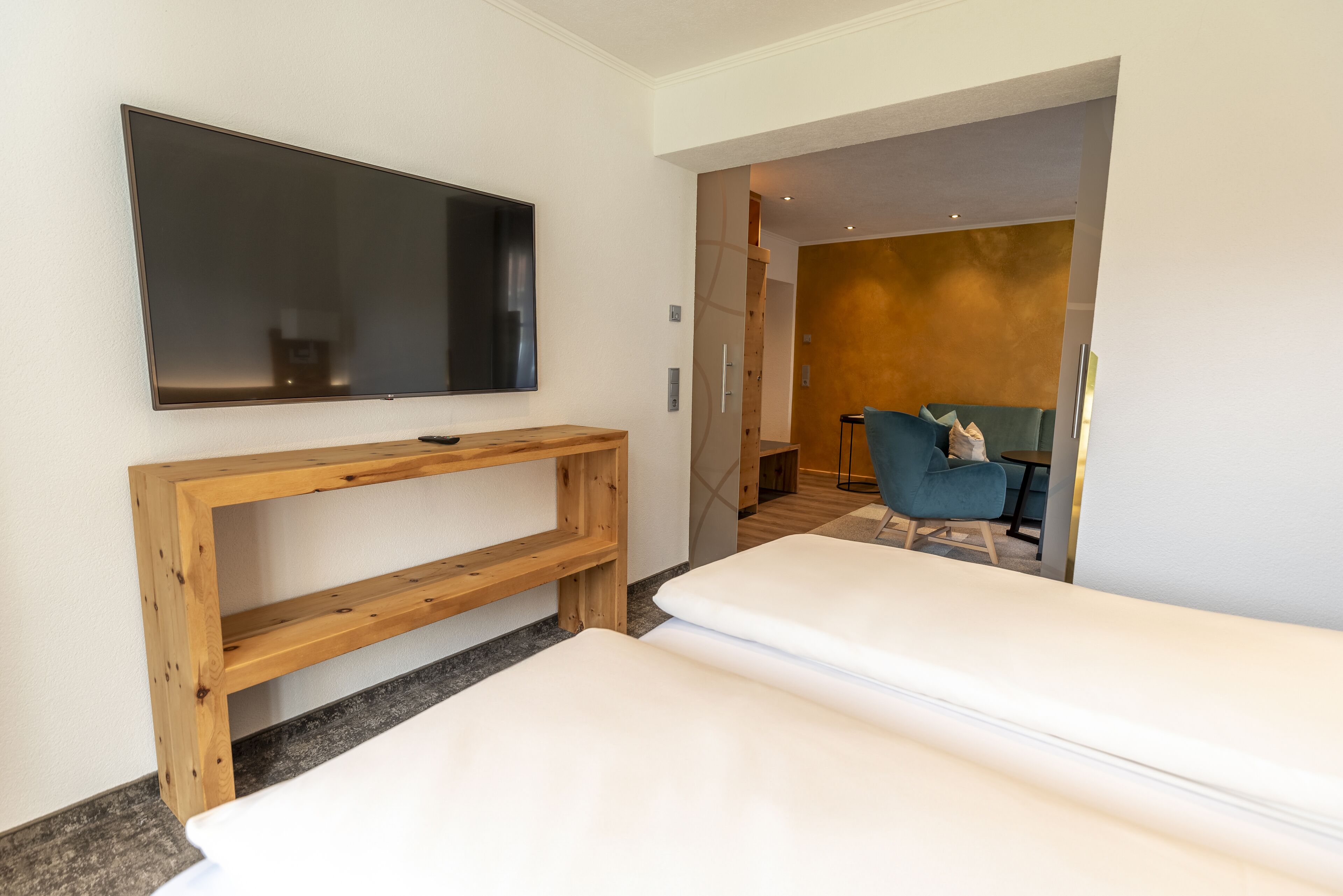 Una habitación de hotel moderna con una televisión de pantalla plana montada en la pared, un banco de madera y un sofá.