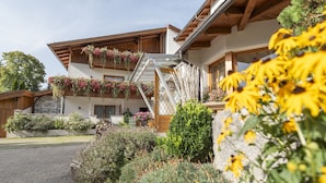 A two-story building with a wooden facade, a staircase with metal railings, and flower boxes on the balconies. - Hotel Arnika (Oberammergau)