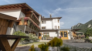 A two-story building with a wooden balcony and flower boxes, a front porch with a bench, and a mountain backdrop. - Hotel Arnika (Oberammergau)
