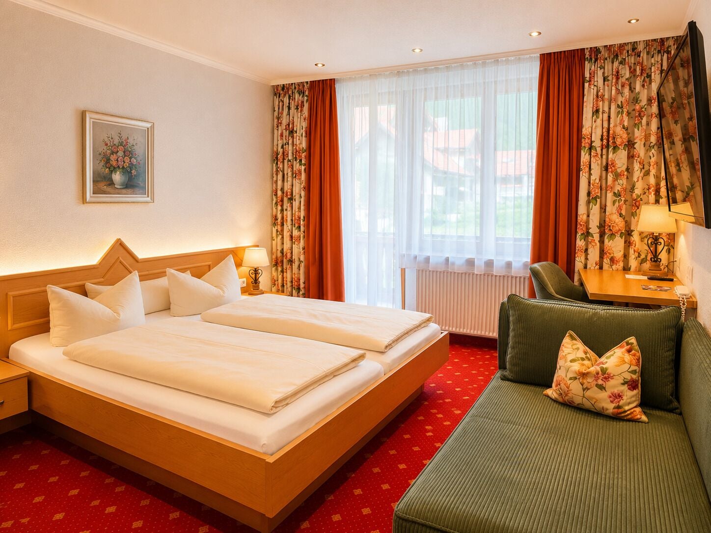 A hotel room with a double bed, a sofa, a table, and a window with curtains.