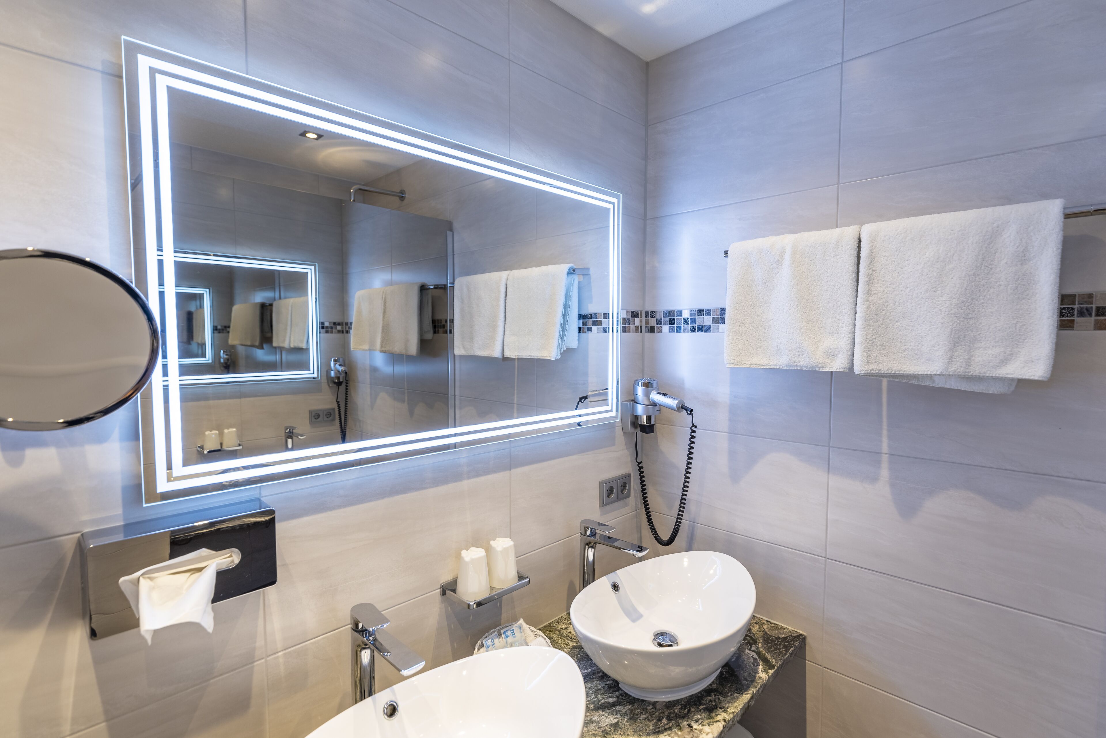 A modern bathroom with two sinks, a large mirror with LED lighting, and neatly arranged towels.