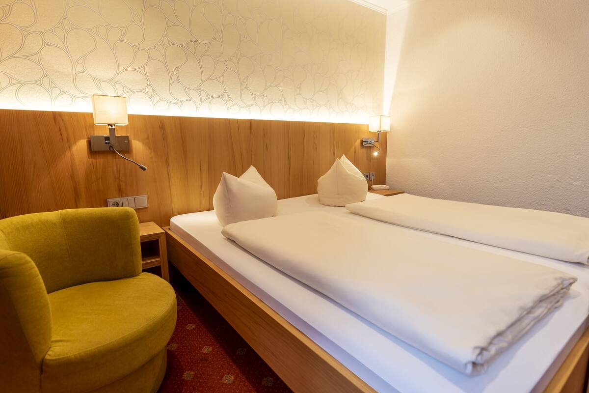 A hotel room with a wooden headboard, two beds with white linens, a yellow armchair, and a patterned wall.