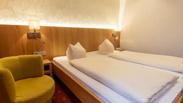 Habitación de hotel con cabecera de madera, dos camas con ropa blanca, un sillón amarillo y pared con estampado.