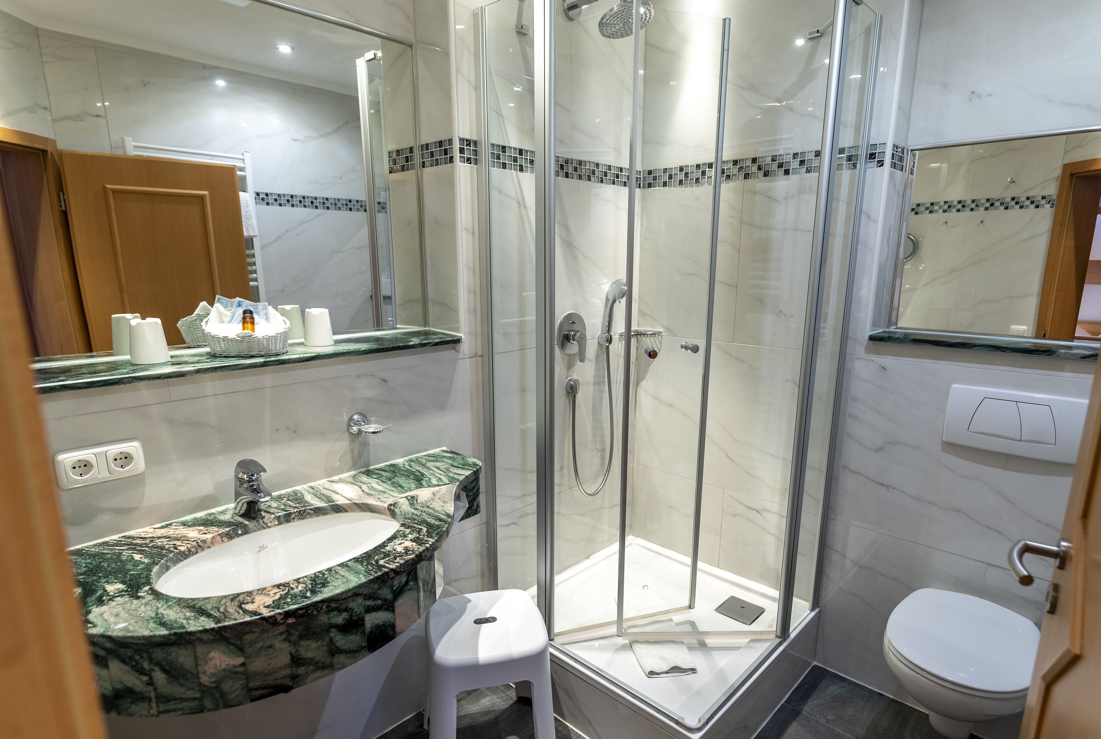 Un baño moderno con ducha de vidrio, lavamanos de mármol y un inodoro blanco.