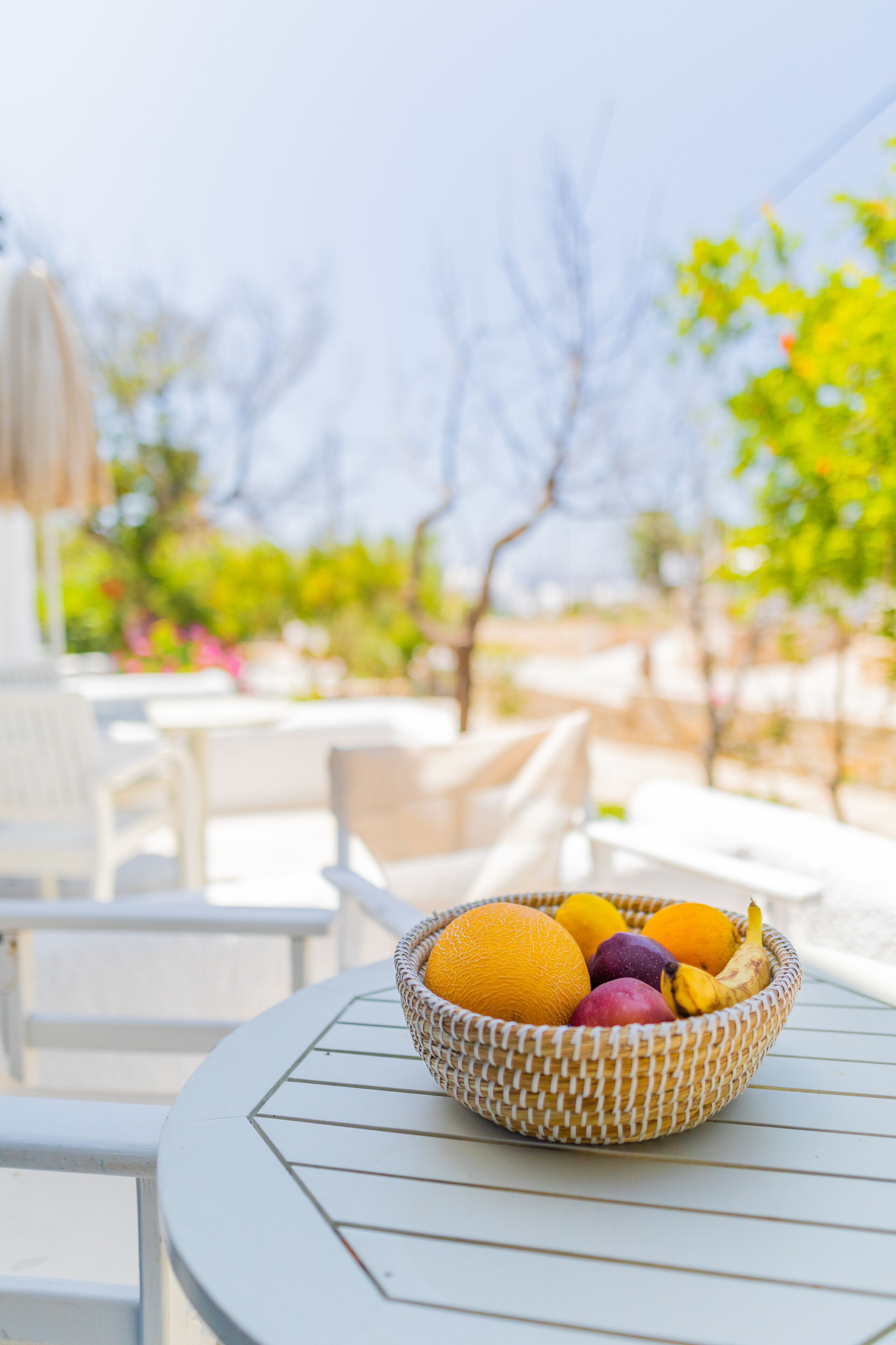 Uma tigela de vime cheia de frutas sobre uma mesa branca ao ar livre.