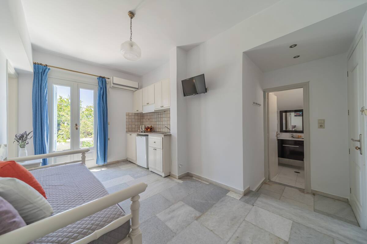 A bedroom with a bed, a bathroom with a mirror, and a kitchen area with cabinets and a TV.