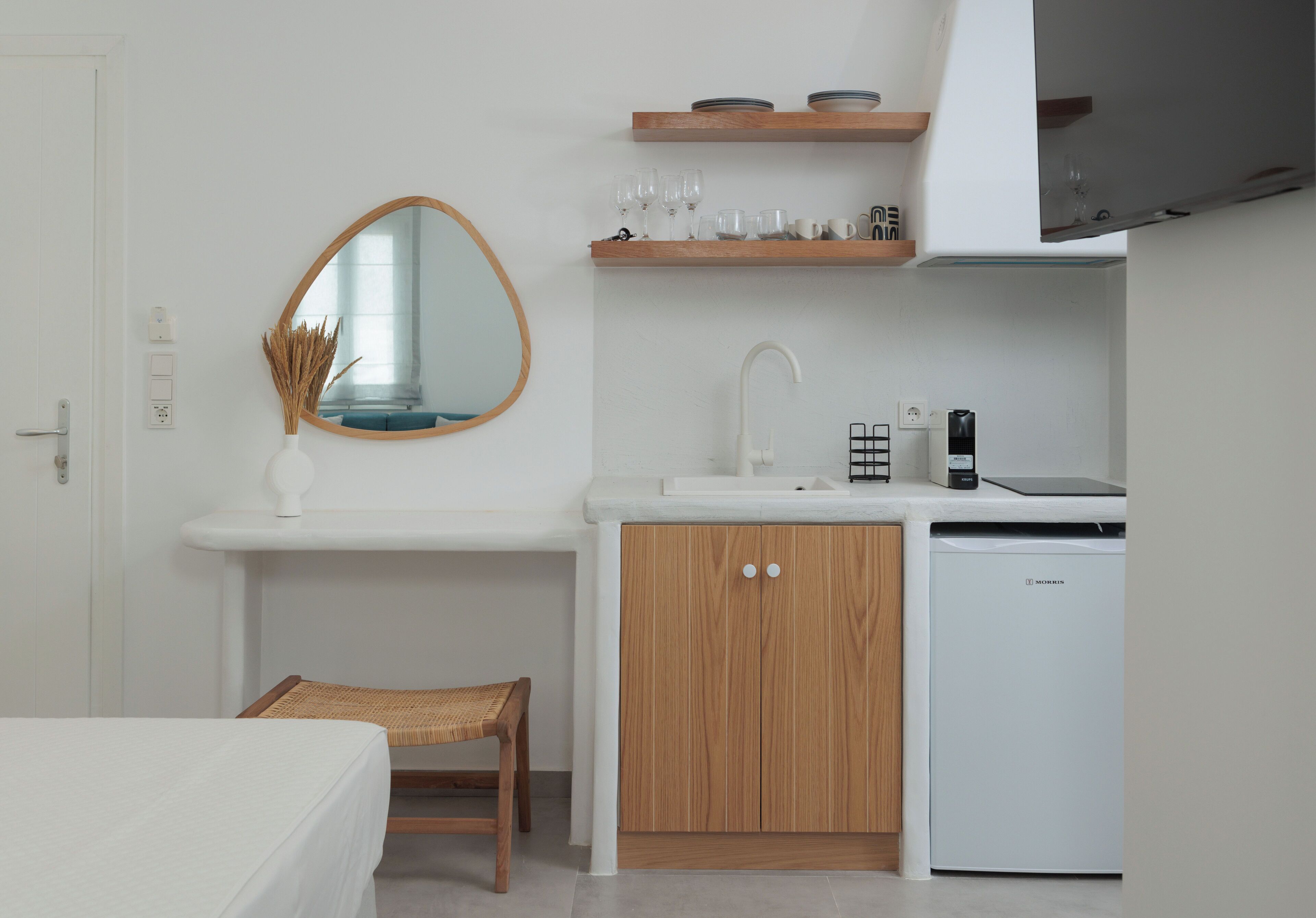 A compact kitchen with a white sink, wooden cabinets, a built-in dishwasher, and a small countertop with glassware.