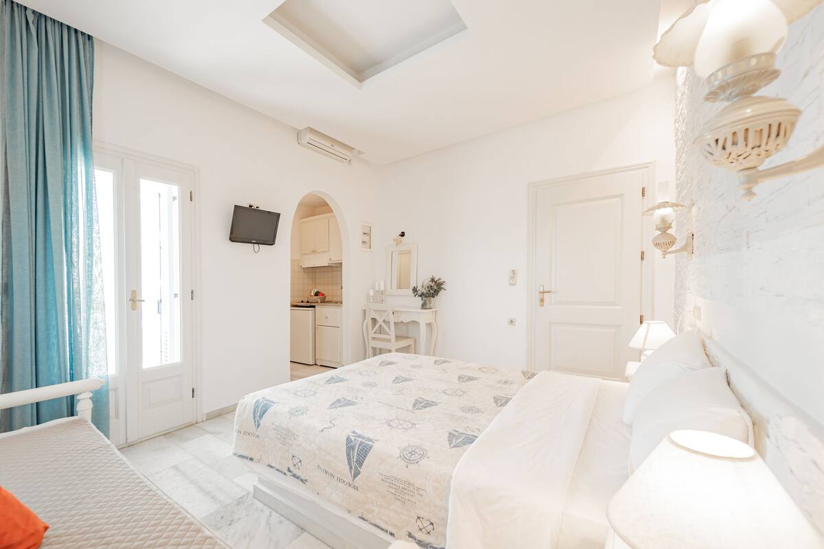 A bedroom with a bed, a desk, a chair, a TV, and a bathroom visible through an archway.