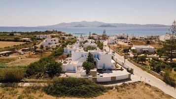 Uma vila costeira com edifícios brancos, uma estrada e vista para o mar e montanhas ao fundo.