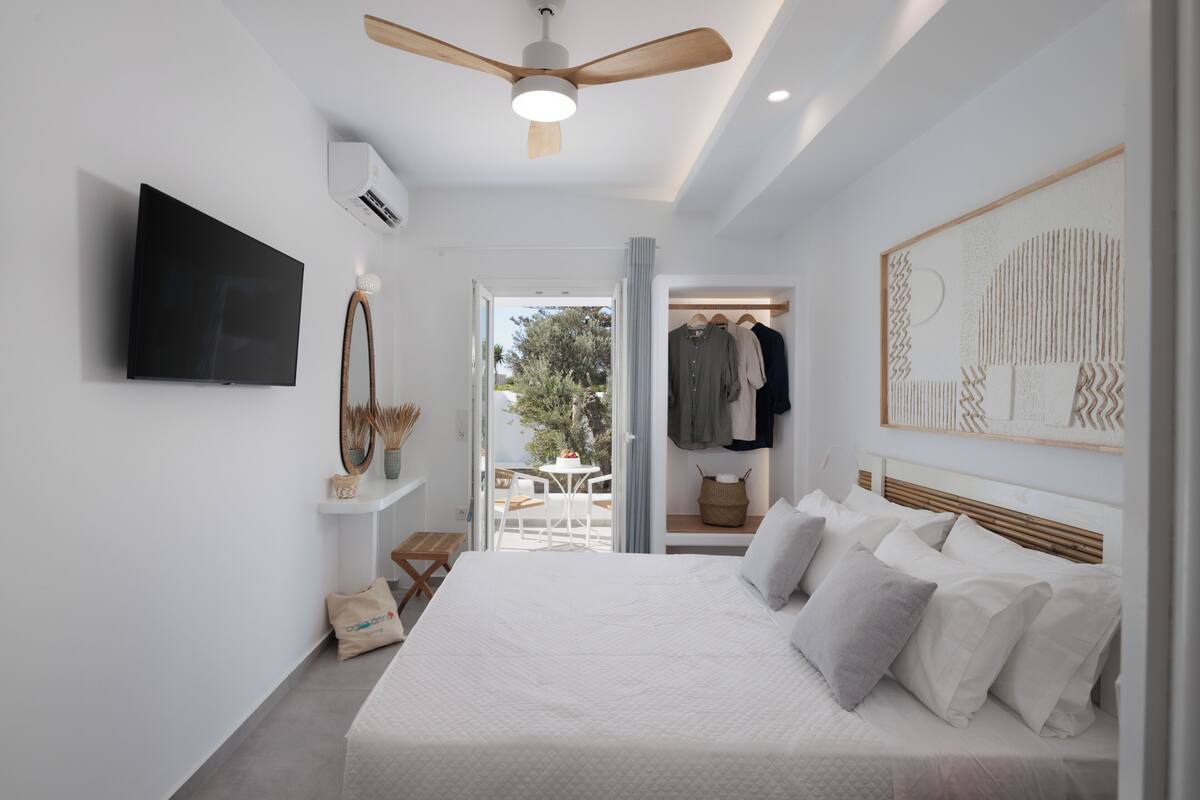 A modern bedroom with a large bed, a ceiling fan, a mounted TV, and a view of the outdoors.