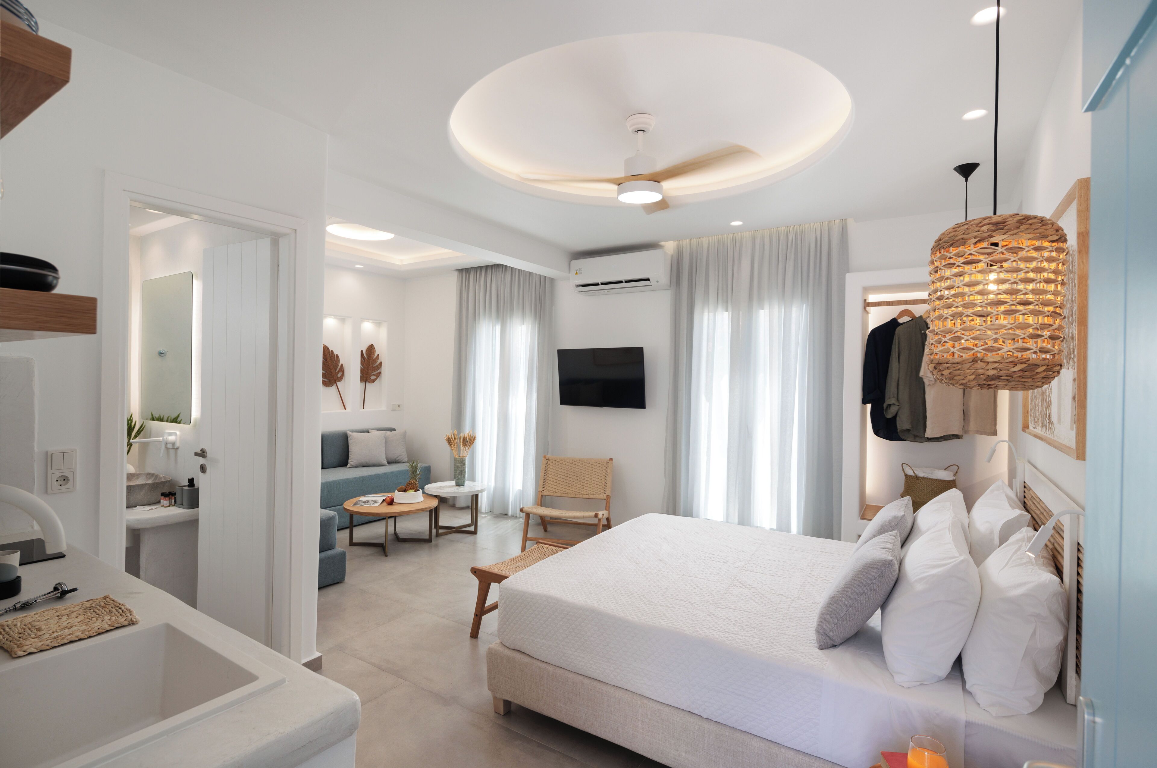 Quarto de hotel moderno com uma cama grande, televisão de tela plana, ventilador de teto e área de jantar com mesa e cadeiras.