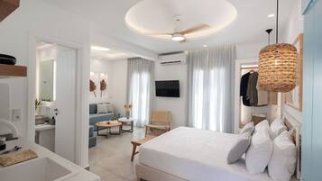 Quarto de hotel moderno com uma cama grande, televisão de tela plana, ventilador de teto e área de jantar com mesa e cadeiras.