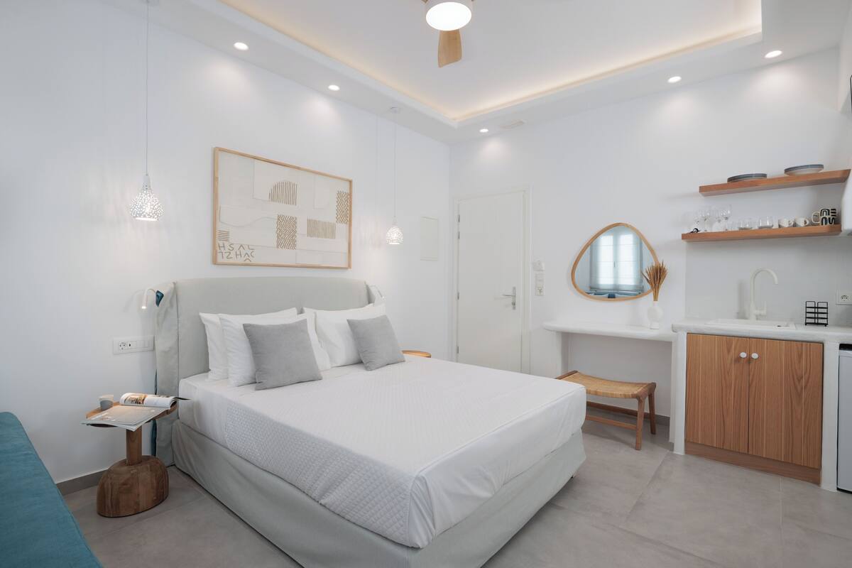 A modern bedroom with a large bed, bedside table, and a small desk area with a mirror and shelves.