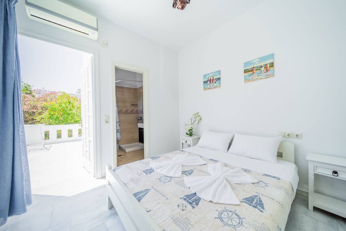 A bedroom with a bed, a nightstand, a wall-mounted air conditioner, and a door leading to a balcony.