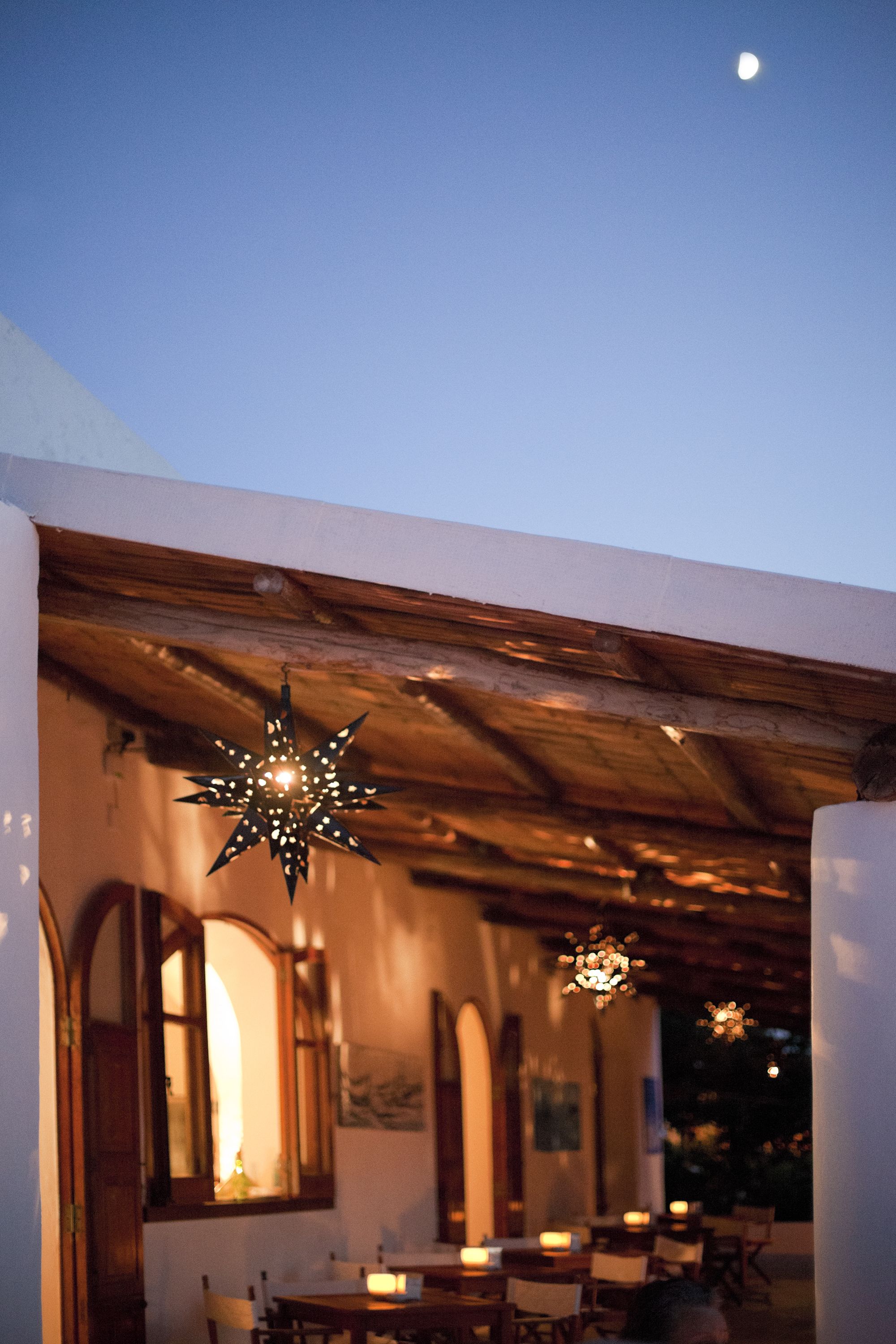 An outdoor dining area with a wooden pergola, hanging star-shaped lights, and a view of the moon.