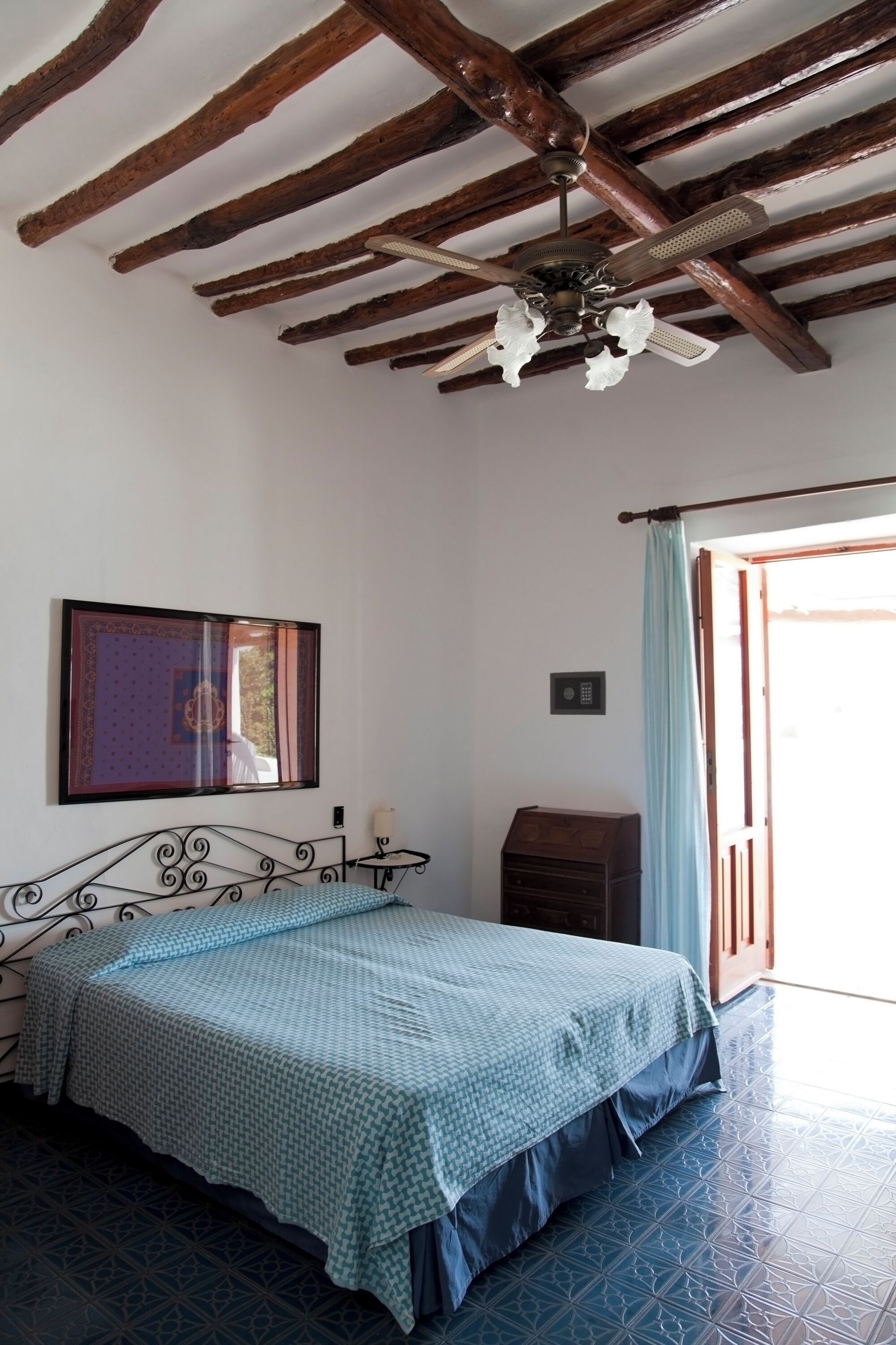A bedroom with a bed, a ceiling fan, a window with curtains, and a door.