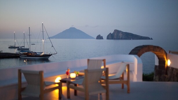 Una terraza frente al mar con vistas al océano, barcos y una montaña a lo lejos.