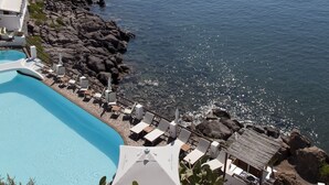 Un hotel frente al mar con piscina, sillas de descanso y sombrillas.