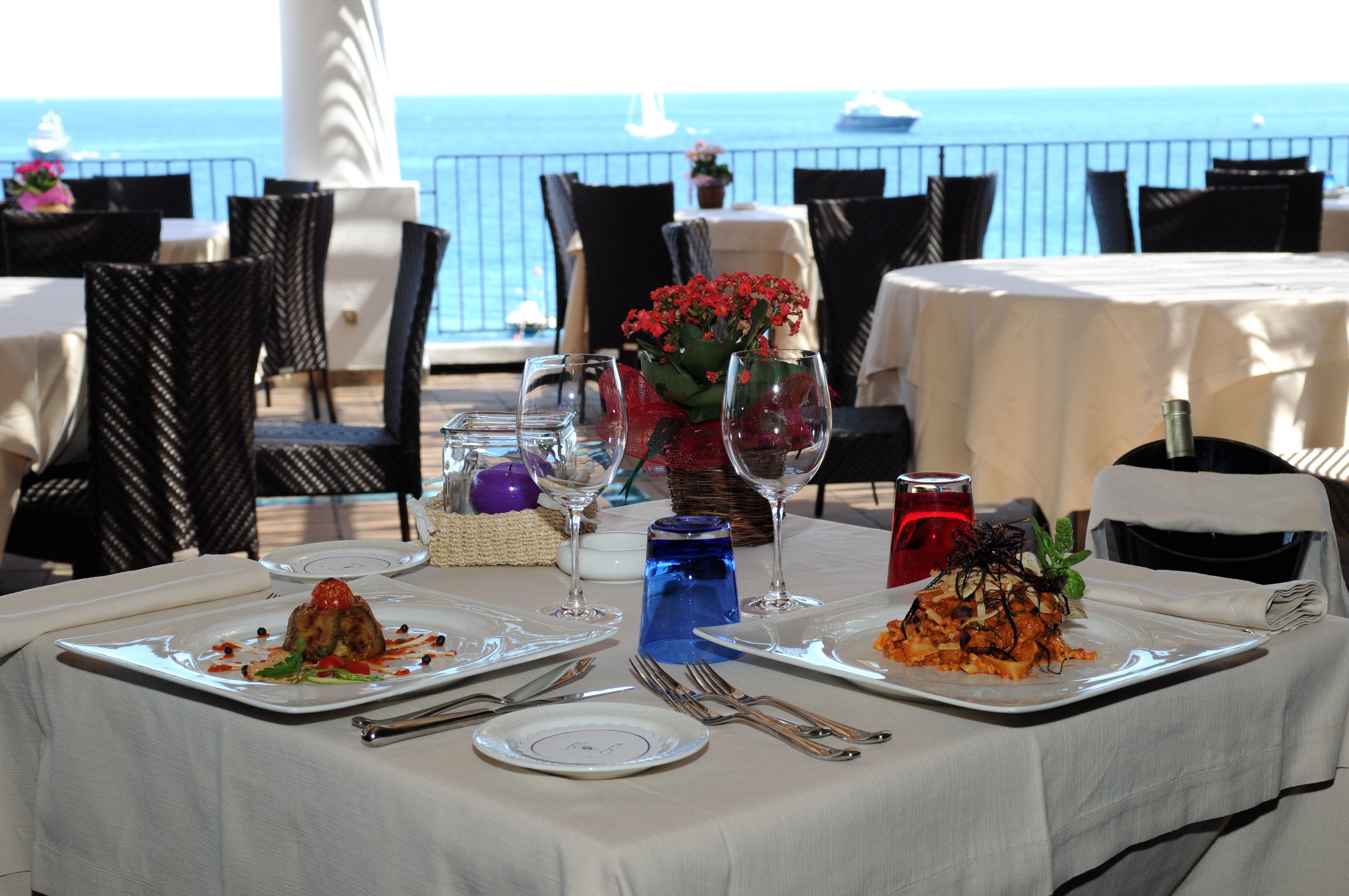 A table set for two with plates of food, cutlery, and a blue glass bottle.
