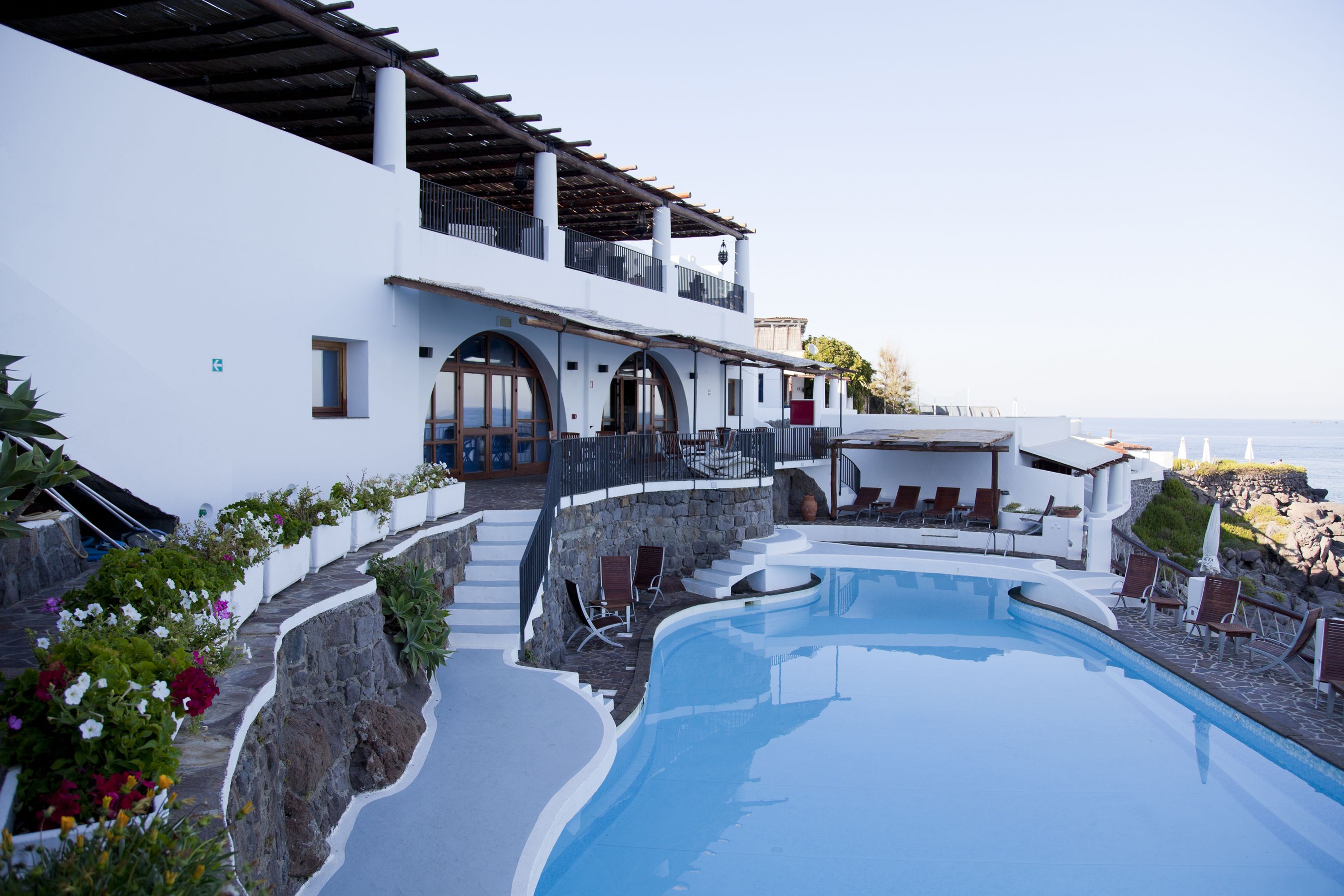 A modern resort with a large pool, outdoor seating, and a view of the sea.
