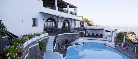 A modern resort with a large pool, outdoor seating, and a view of the sea.