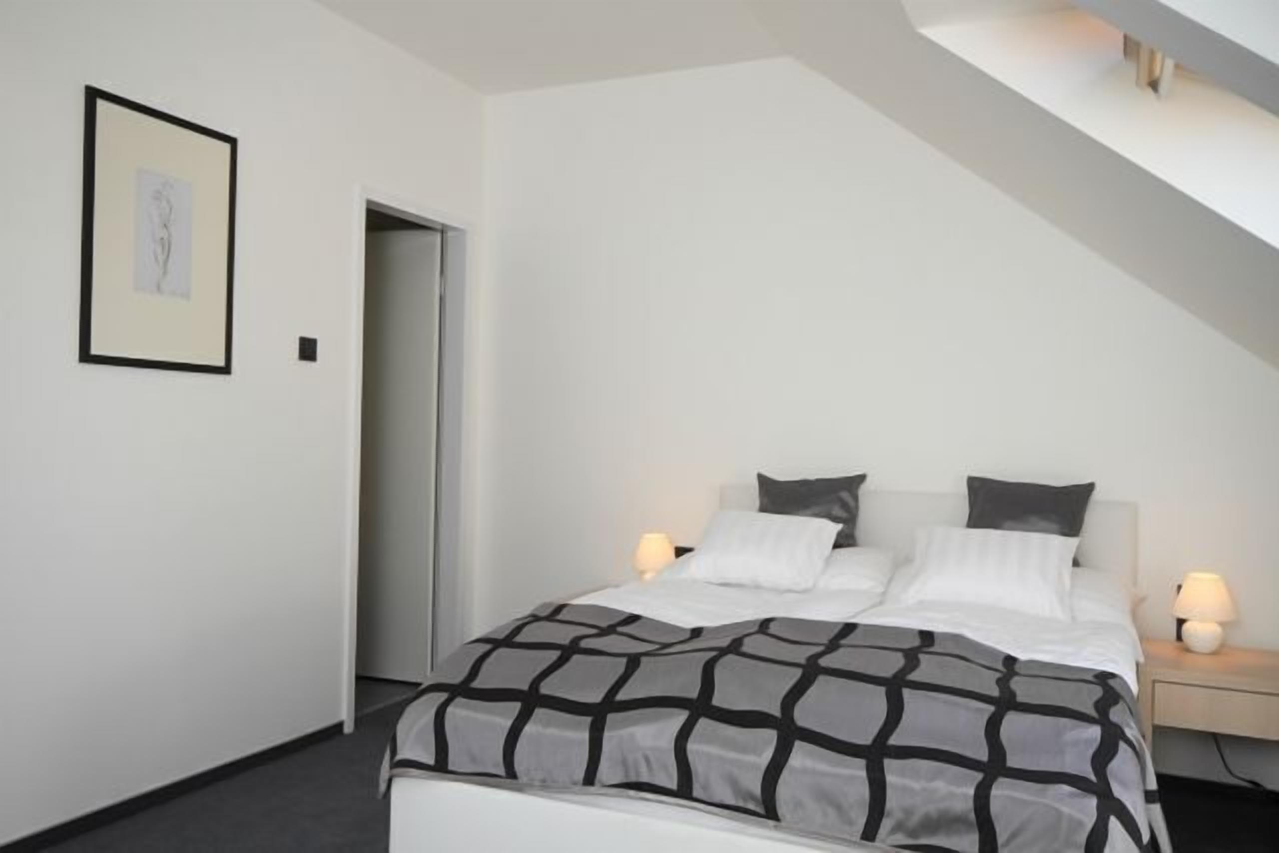 A bedroom with a bed, bedside lamps, a framed picture on the wall, and a door.