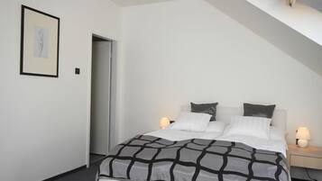 A bedroom with a bed, bedside lamps, a framed picture on the wall, and a door.
