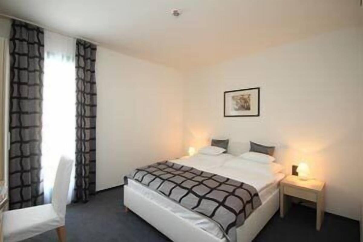 Habitación de hotel con una cama, una silla, una mesita de noche y un cuadro colgado en la pared.