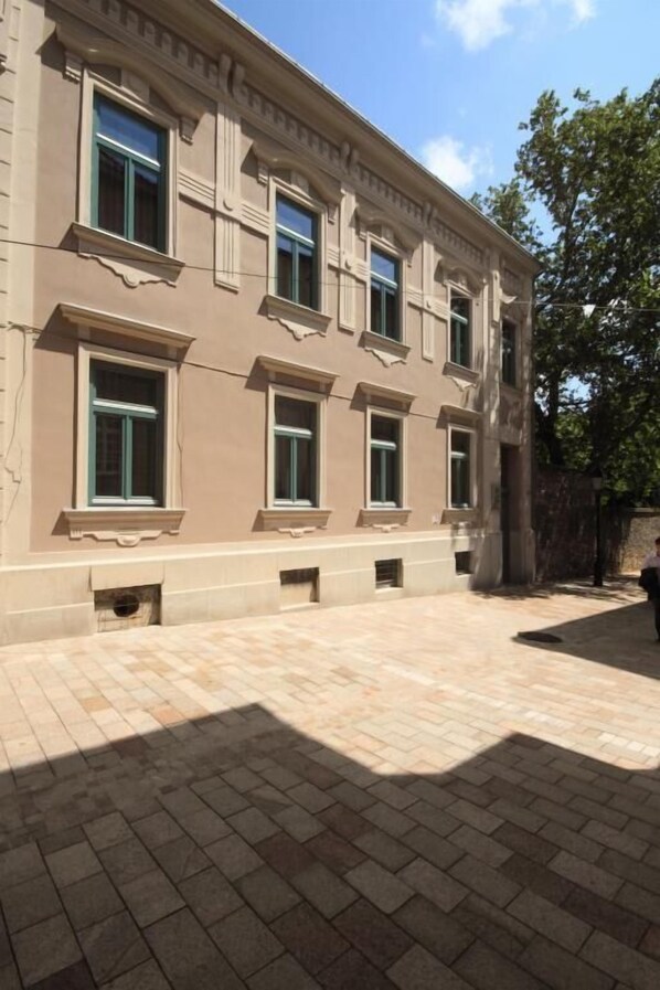 Un edificio con fachada simétrica, varias ventanas y un patio empedrado.