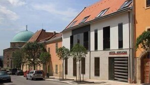 A street view with a building labeled "HOTEL AMARADA" featuring a modern facade, a dome structure in the background, and parked cars along the road. - Hotel Arkadia (Pecs)
