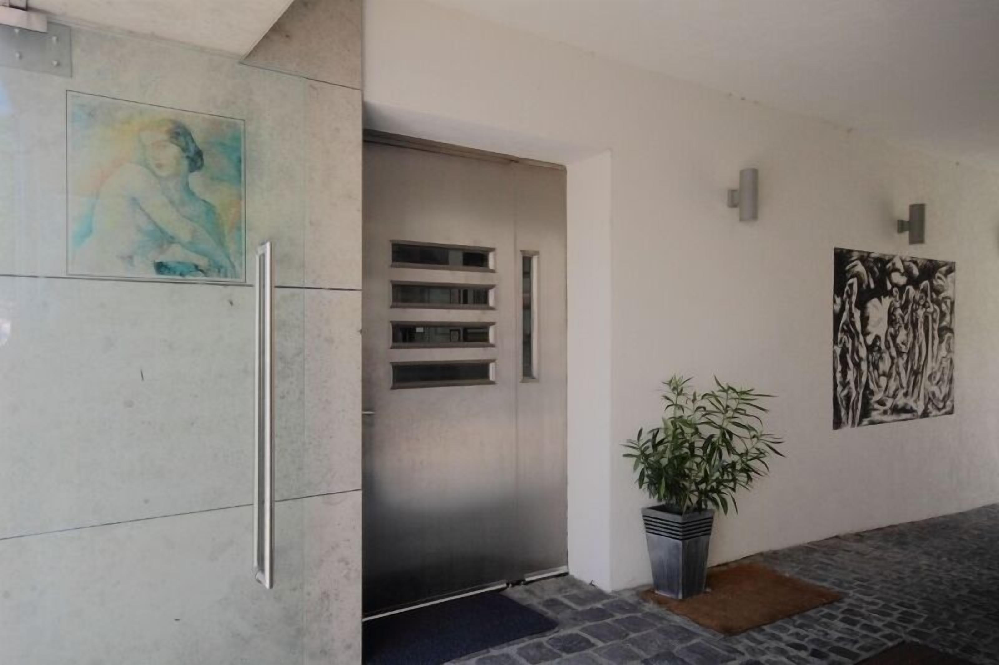 Un ingresso moderno con una porta metallica, una pianta in vaso e due opere d'arte alle pareti.