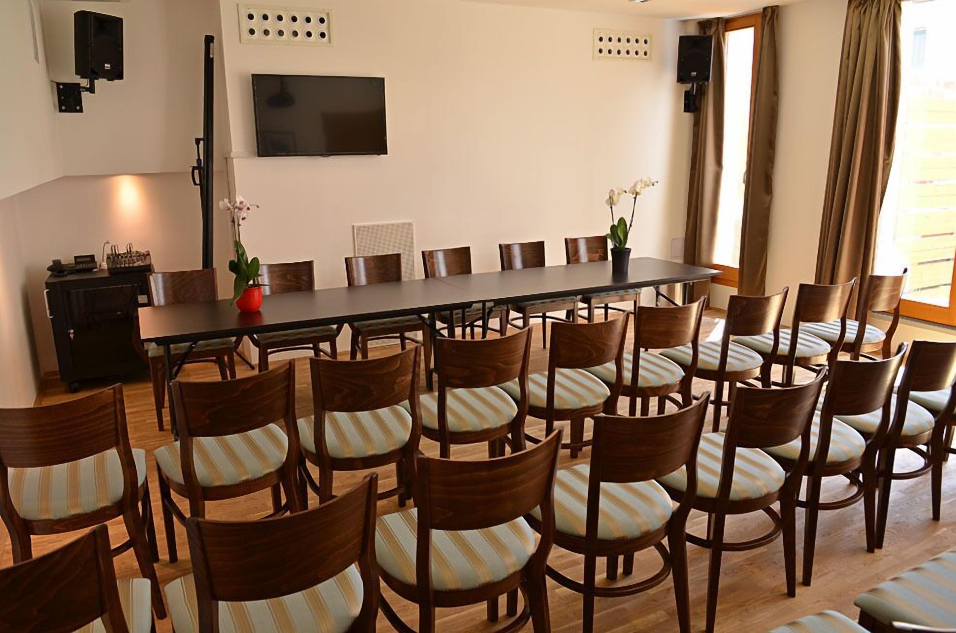A conference room with a long table and multiple chairs, a television on the wall, and a window with curtains.