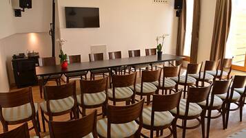 A conference room with a long table and multiple chairs, a television on the wall, and a window with curtains.