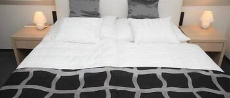 Una cama con una colcha de diseño blanco y negro, dos almohadas y dos lámparas de noche a cada lado.