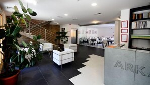A modern lobby with a staircase, seating area, and a reception desk labeled 'ARK'. - Hotel Arkadia (Pecs)
