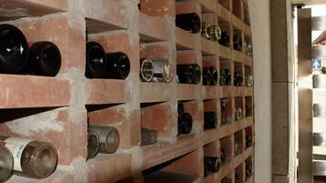 A brick wine cellar with multiple shelves holding wine bottles.